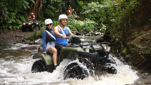 Couple riding an ATV through a shallow river during a rainforest tour in La Fortuna, Costa Rica.